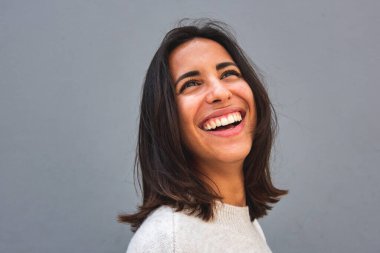 Gri arkaplanlı, gülen genç bir kadının yan portresi. 