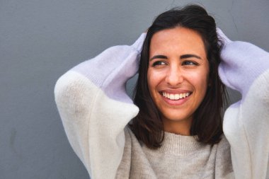 Kapalı portre güzel genç kadın elleri saçlarında gülümsüyor ve gri arka plandan başka tarafa bakıyor.