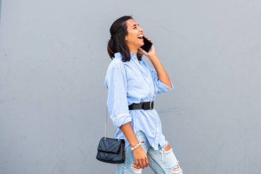Gri duvarda cep telefonuyla konuşan genç bir kadının yan portresi.