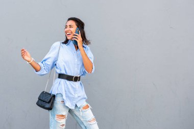 Mutlu genç bir kadının portresi cep telefonuyla konuşuyor ve gri arka planda dönüp duruyor. 