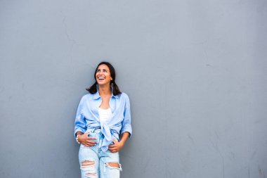 Gri duvara yaslanıp başka tarafa bakarken gülen güzel bir genç kadının portresi.