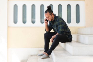 Dışarıda merdivenlerde otururken cep telefonuyla konuşan mutlu adam.