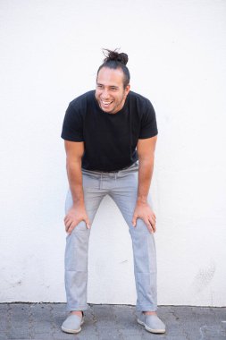 Parlak güneşli bir günde saçlarını topuz gibi toplayarak dışarıda eğilen gülen adam.