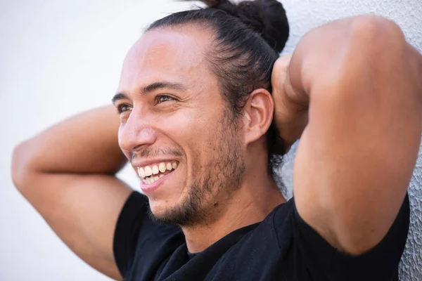 Cheerful man with pulled up hair bun and hands behind head over white background