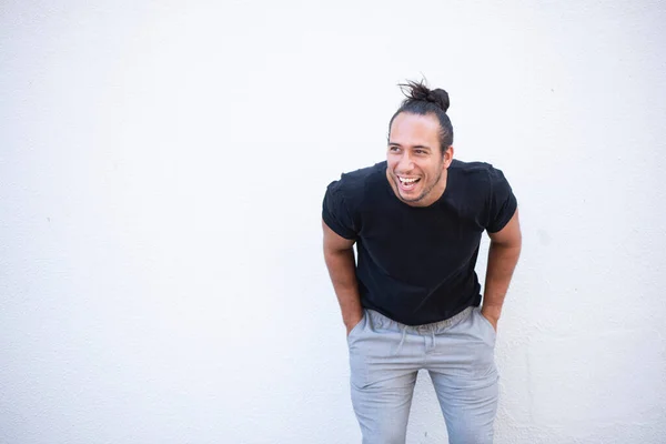 Cheerful man with pulled up hair bun and hands in pocket bending over white background