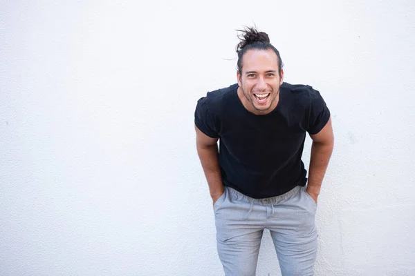 Portrait of cheerful man with pulled up hair bun and hands in pocket bending over white background