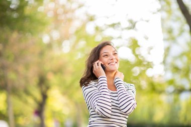 Parkta cep telefonuyla konuşan gülümseyen genç bir kadının portresi 