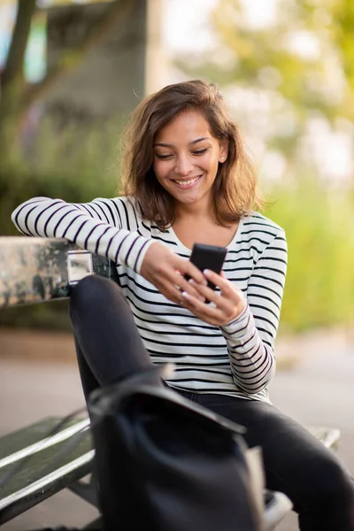 Портрет Улыбающейся Молодой Женщины Сидящей Скамейке Парке Смотрящей Мобильный Телефон — стоковое фото