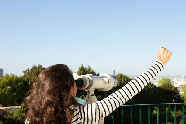 Arkasından teleskopla şehir manzarasına bakan genç bir kadının portresi.