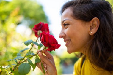 Dışarıda kırmızı güller kokan gülümseyen genç bir kadının yan portresi. 
