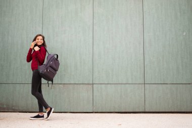 Çantasıyla yürüyen ve cep telefonuyla konuşan genç bir kadının tam boy profil portresi