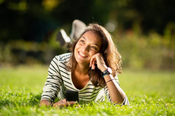 携帯電話で公園でリラックス魅力的な若い女性の肖像画 — ストック写真