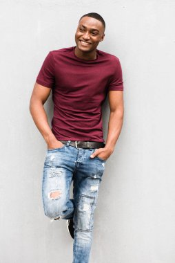 Gülümseyen Afrikalı Amerikalı adamın portresi gri duvarda poz veriyor ve başka tarafa bakıyor.