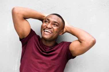Elleri kafasının arkasında gri duvara yaslanmış mutlu Afro-Amerikan genç bir adamın portresini yakından çek.