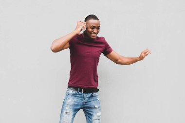 Kulaklıkla müzik dinleyen ve gri duvarda dans eden mutlu Afrikalı Amerikalı adamın portresi.