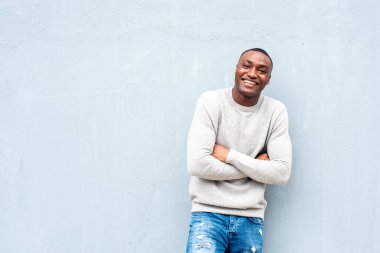 Kollarını kavuşturarak duvara yaslanan gülümseyen Afrikalı Amerikalı adamın yatay portresi.