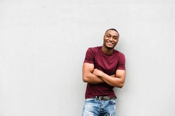 一个年轻英俊的非裔美国人靠着灰色的墙壁 双手交叉地微笑的画像 — 图库照片