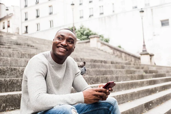 Boczny Portret Uśmiechniętego Afroamerykanina Siedzącego Zewnątrz Mieście Telefonem Komórkowym — Zdjęcie stockowe