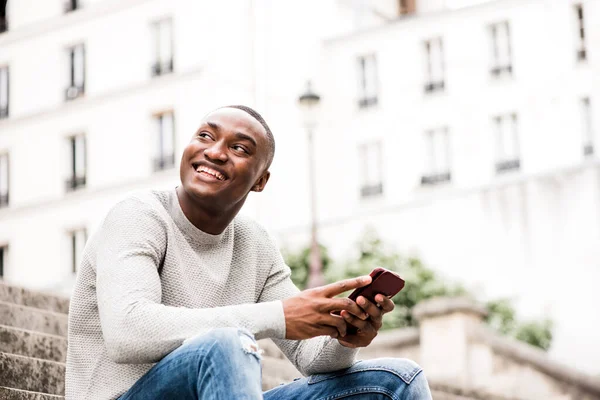 Boczny Portret Uśmiechniętego Afroamerykanina Siedzącego Zewnątrz Mieście Trzymającego Komórkę — Zdjęcie stockowe