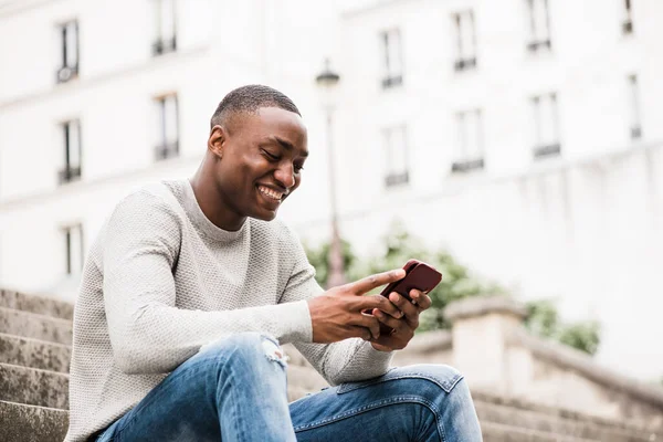 携帯電話を使って街の外に座っているアフリカ系アメリカ人の笑顔のサイドポートレート — ストック写真