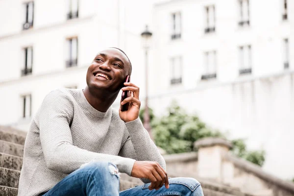 Boczny Portret Uśmiechniętego Afroamerykanina Siedzącego Zewnątrz Mieście Rozmawiającego Telefonem Komórkowym — Zdjęcie stockowe