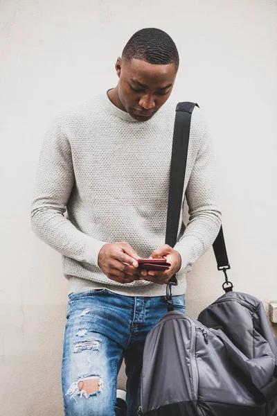 Portret Afroamerykanina Korzystającego Telefonu Komórkowego Stojącego Przy Białej Ścianie Torbą — Zdjęcie stockowe
