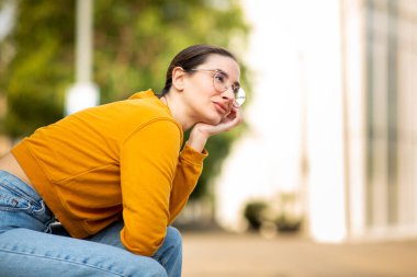 Güzel bir genç kadının portresi dışarıda oturuyor, başka tarafa bakıyor ve eli çenesinde düşünüyor.