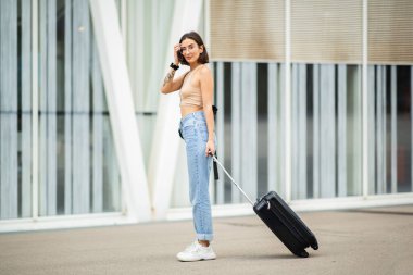 Sokakta elinde bavulla kameraya bakan güzel bir gencin tam boy portresi.