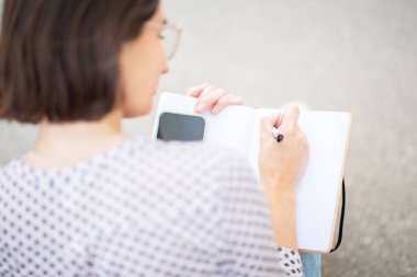 Omzunun üstünden. Kapalı. Dışarıda oturan bir kadının kitap yazması.