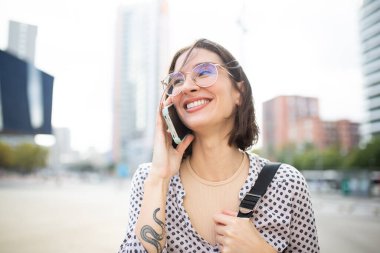 Dışarıda yürüyen, cep telefonuyla konuşan, yüzünü çeviren ve gülümseyen güzel bir genç kadının yakın portresi.