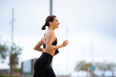 Kentte sabah spor giyim içinde koşan aktif genç bir kadının yan portresi.