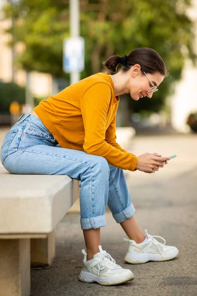 Портрет Молодой Женщины Сидящей Скамейке Снаружи Пользующейся Мобильным Телефоном — стоковое фото