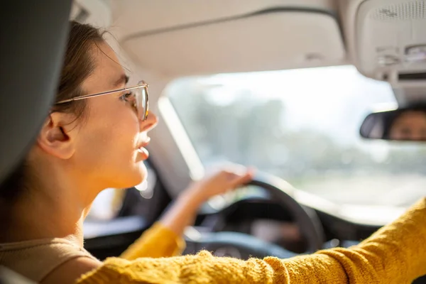 Rear view portrait of young female commuter adjusting inside rear view mirror while driving car in the city