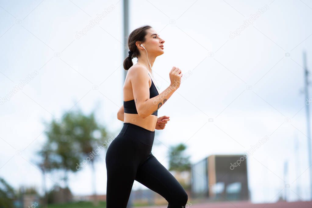 Side portrait of fitness woman wearing earphones doing running workout outside in morning