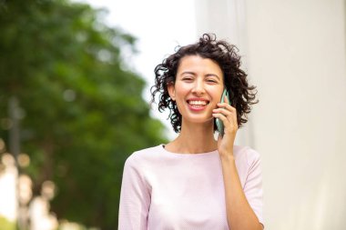 Dışarıda cep telefonuyla konuşan neşeli genç bir kadının portresi.