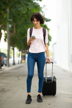 Mutlu kadın bavulu çekiyor ve cep telefonuna mesaj atıyor.