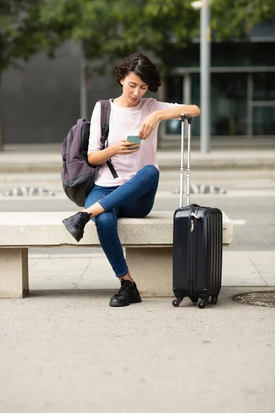 荷物を持って屋外に座っている間 スマートフォンを使用して女性旅行者メッセージ — ストック写真
