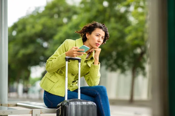 在城市的公交车站 忧心忡忡的女人拿着智能手机和行李等待着 — 图库照片