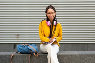 Güzel, Afro-Amerikan bir kızın portresi. Elinde bir kitapla dışarıda oturuyor.