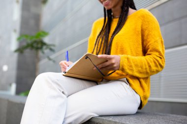 Kalem ve kitapla çalışan bir kadının dışarıda otururken çekilmiş portresi. 