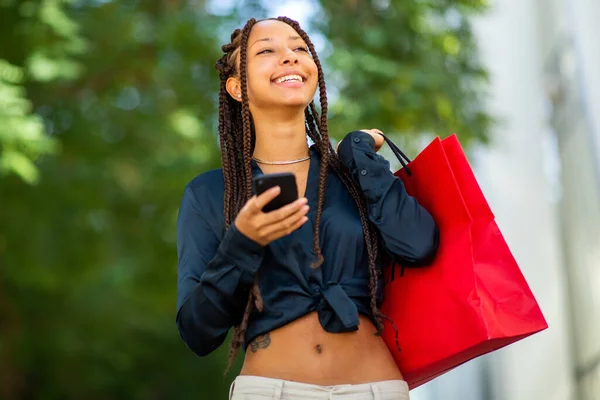 美しい若いアフリカ系アメリカ人女性の携帯電話やショッピングバッグの肖像画市内の外 — ストック写真