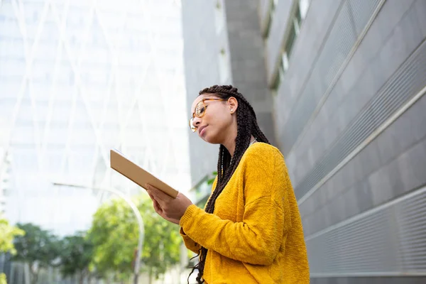 Dışarıda oturmuş, gözlük takıp kitap okuyan, örgülü saçlı Afro-Amerikalı bir kızın portresi.