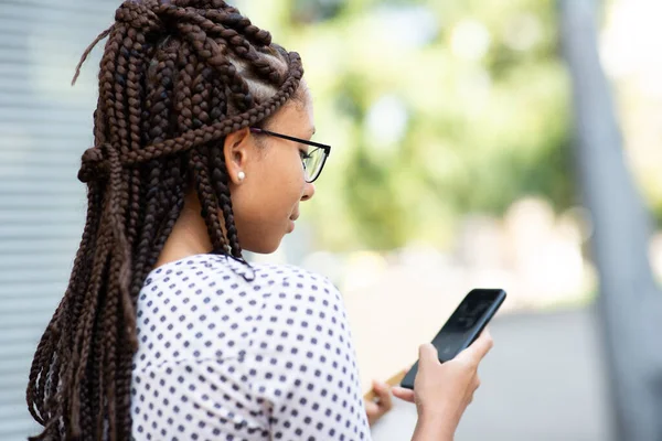閉じますアップポートレートの若いですアフリカの女性とともに編組髪身に着けている眼鏡テキストの彼女の携帯電話で外 — ストック写真