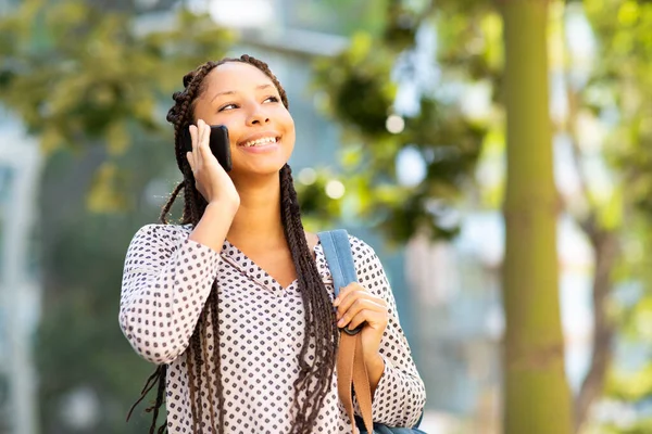 Elinde çantasıyla dışarıda cep telefonuyla konuşan gülümseyen zenci kadının yakın plan portresi.