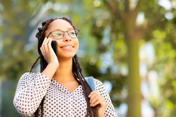 Gözlüklü ve çantalı gülümseyen Afrikalı Amerikalı kızın cep telefonuyla konuşurken yakın plan portresi.