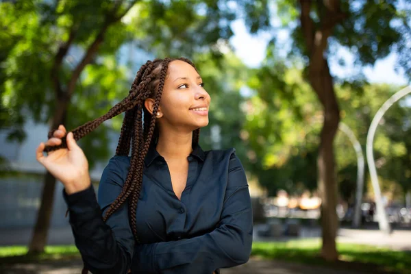Side portrait of beautiful young African American woman with braided hairstyle standing outside and looking away