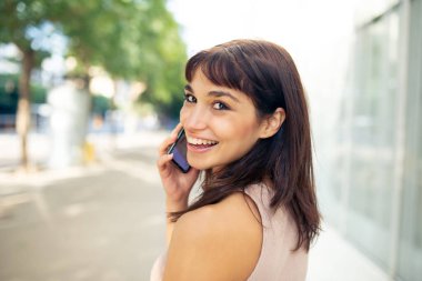 Şehirde arkasına bakıp cep telefonuyla konuşan güzel bir genç kadının portresini yakından çek.