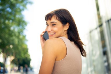 Güzel genç bir kadının yakın portresi. Arkaya bakıyor ve şehirde cep telefonuyla konuşuyor.