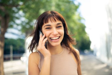 Şehrin dışında cep telefonu kullanan neşeli genç bir kadının portresini kapat.