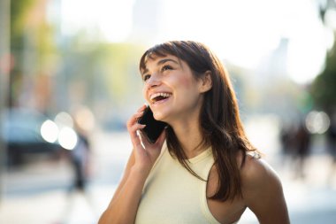 Şehrin dışında dikilirken telefonla konuşan neşeli genç bir kadının portresini kapat.